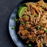 Traditional pad thai noodle dishes with bean sprouts and cashew nuts with a lime wedge.