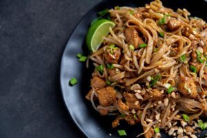 Traditional pad thai noodle dishes with bean sprouts and cashew nuts with a lime wedge.