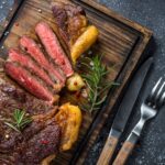 grilled beef steak ribeye on wooden cutting board dressed with chimichurri and onion ring