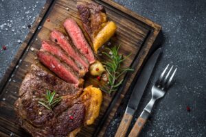 grilled beef steak ribeye on wooden cutting board dressed with chimichurri and onion ring